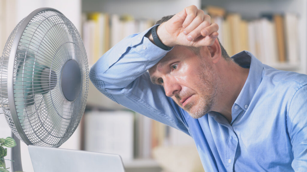 A man sweats due to the heat and tries to cool off by a fan. (iStock image)