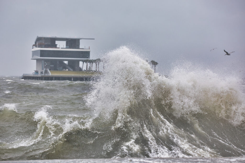 A wave crashing against a seawall on Tampa Bay during a tropical storm with the St Pete Pier in the background. (iStock image)