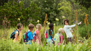 A young teacher with children on a nature field trip. Moving away from the structures and competition of indoor classroom settings matters for students. (iStock image)